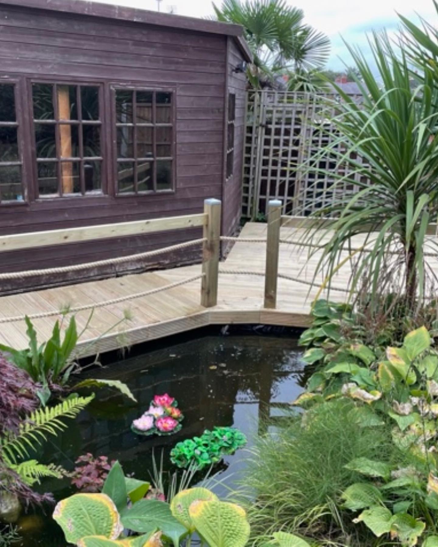 a pond with flowers in it and a wooden bridge in front of a building